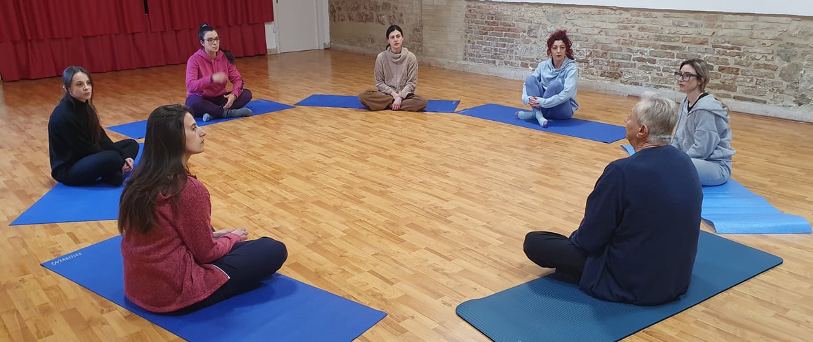 a group of people sitting on yoga mats in a circle, classe di esercizi di bioenergetica
