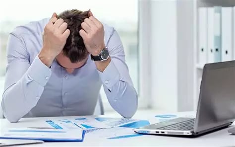 Homme stressé tête baissée avec coudes sur son bureau et ses deux mains sur sa tête