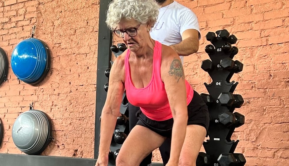 mulher mais velha treinando com auxilio de instrutor de funcional