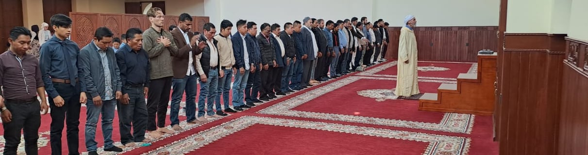 a group of men standing in line performing salat at Imam Malik Mosque