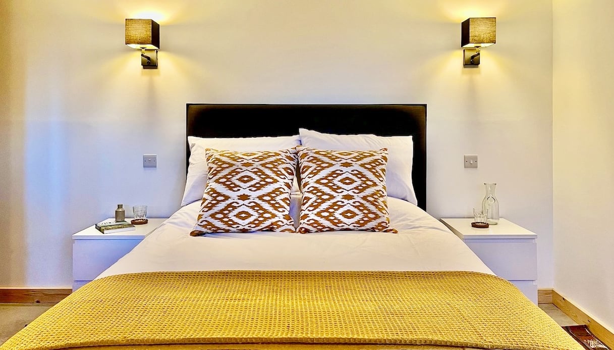 a large bed with wall lights and colourful cushions and throw