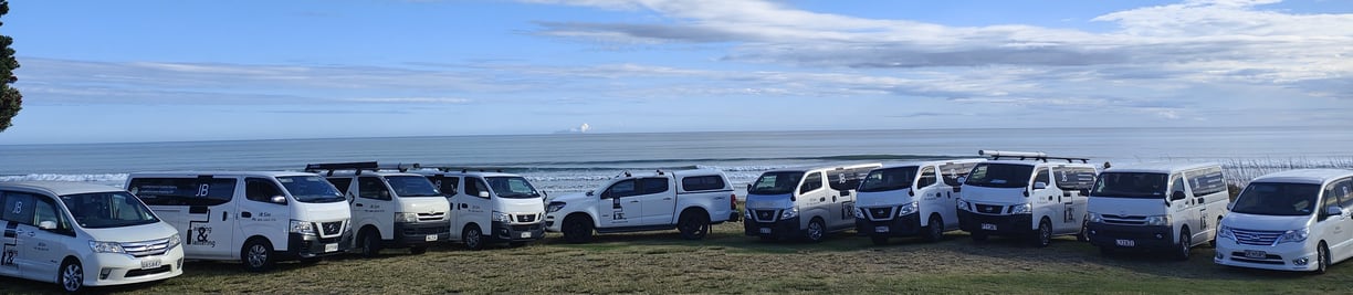 A group of JB Painting & Plastering vans parked in a row in front of the sea.