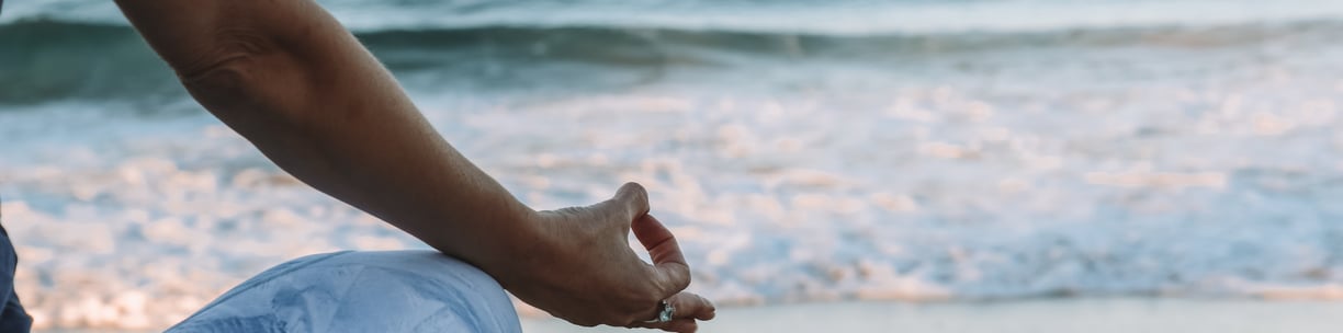Woman meditating on beach. How properly managed stress becomes beneficial. Mindletic Blog