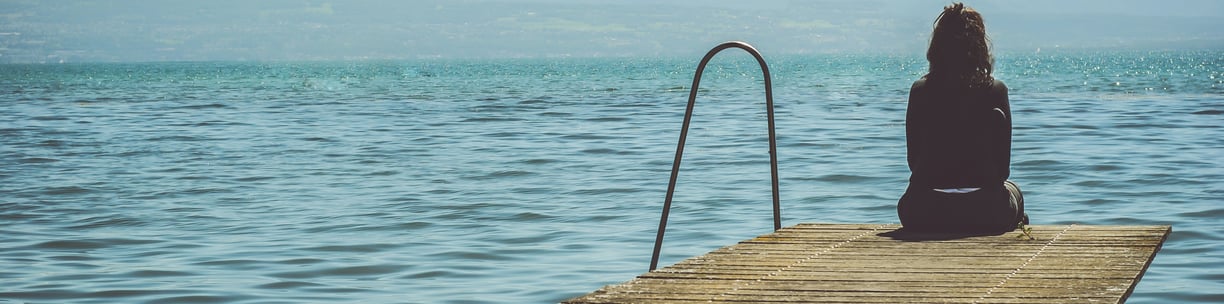 Woman sitting by a lake and looking at the water. How to deal with sadness? Mindletic Blog