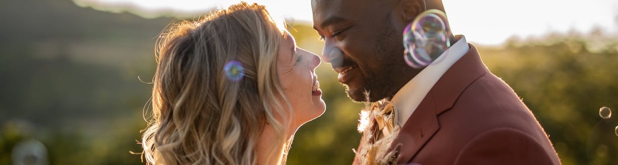 a bride and groom in front of blowing bubbles in the air, in front of the sunset