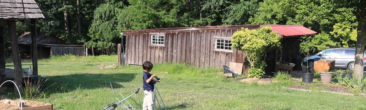 A barn structure in a field with a boy. 