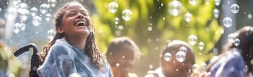 Happy girl in wheelchair laughing outdoors surrounded by bubbles and friends
