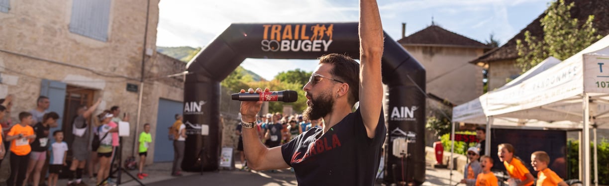 a man in a black shirt speaking with a microphone in a sport event, in front of the starting line