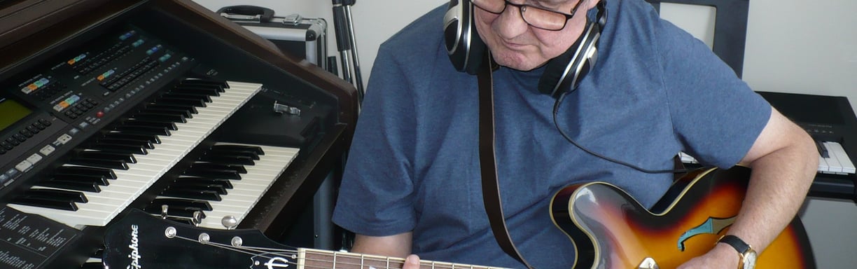 photograph of Julian Sumner with guitar and keyboards in recording studio