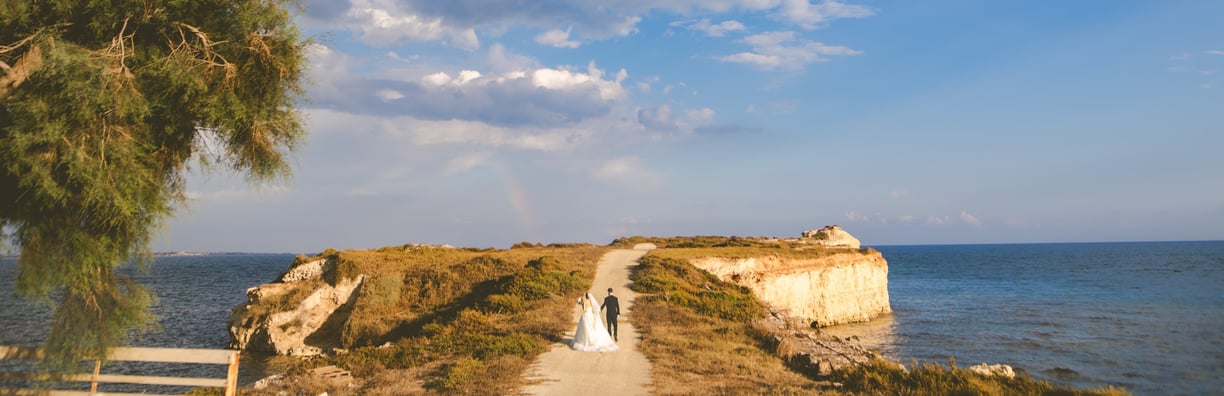 una sposa e uno sposo che camminano lungo un sentiero con arcobaleno