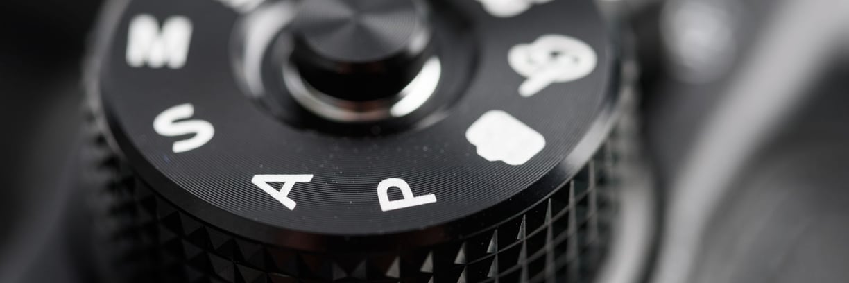 Close-up of a DSLR camera mode dial showing Auto (A), Program (P), settings, symbolising the choice between auto and manual