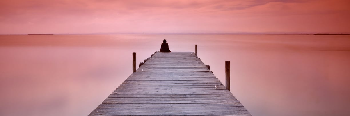 A person sitting alone at the end of a jetty on a calm evening. The scene depicts the Lonely Art of Art