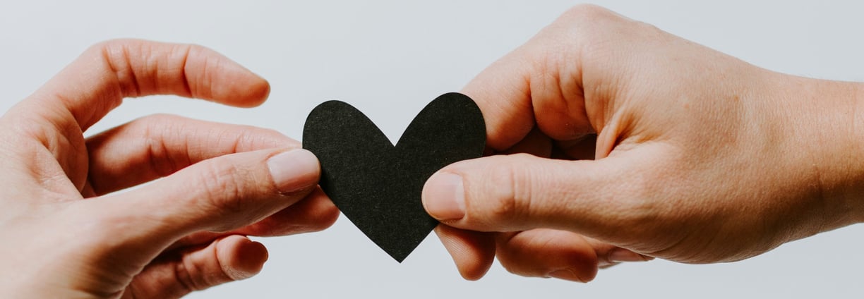 Hands Coming together both holding onto a heart shaped piece of black card
