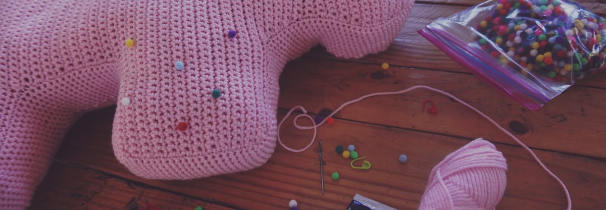 a pink crochet elephant sitting on a table with tools