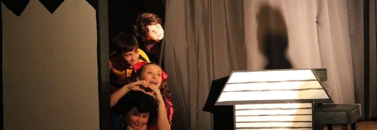 Young children performing a musical on stage in colorful costumes.