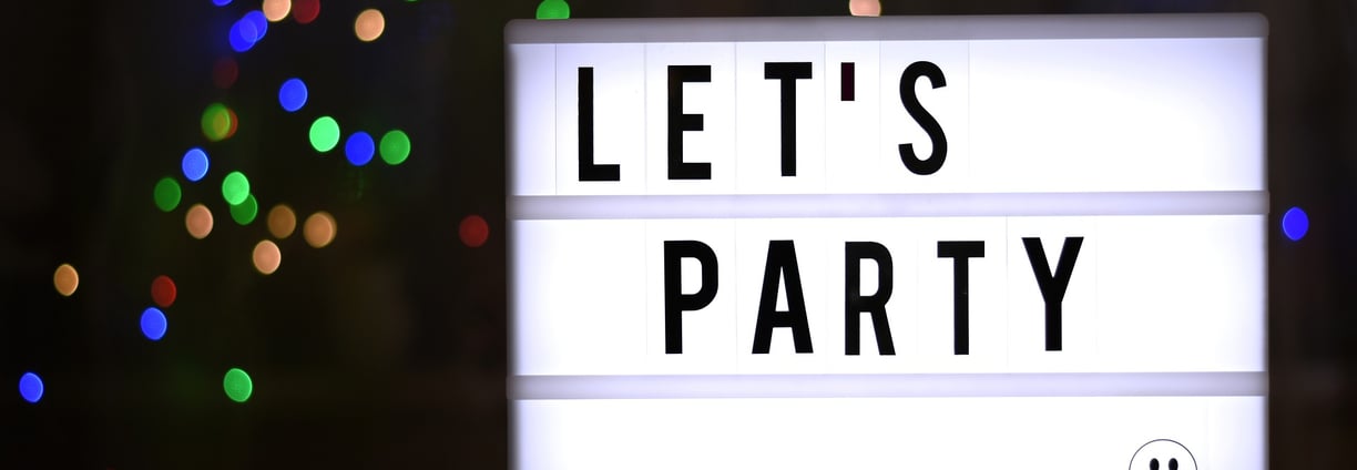 A lit sign in a darkened room that reads "Let's Party"