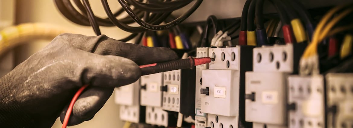 a person holding a wire and wires in front of a wall mounted electrical equipment
