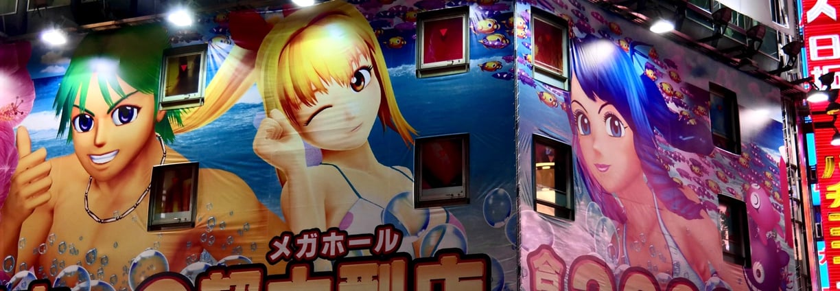 An illuminated building facade is covered with large, colorful anime-style illustrations featuring c