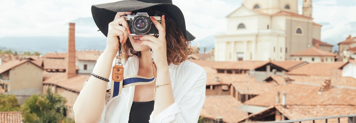  "A traveling woman wearing a stylish hat holding a camera, ready to capture travel moments. 