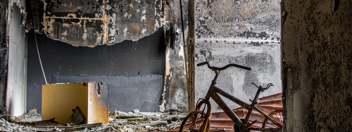 Estancia de una vivienda después de un incendio, se ve bicicleta quemada, paredes y muebles quemados