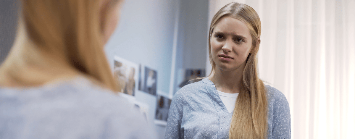 Jeune femme qui se regarde dans le miroir et doute d'elle-même