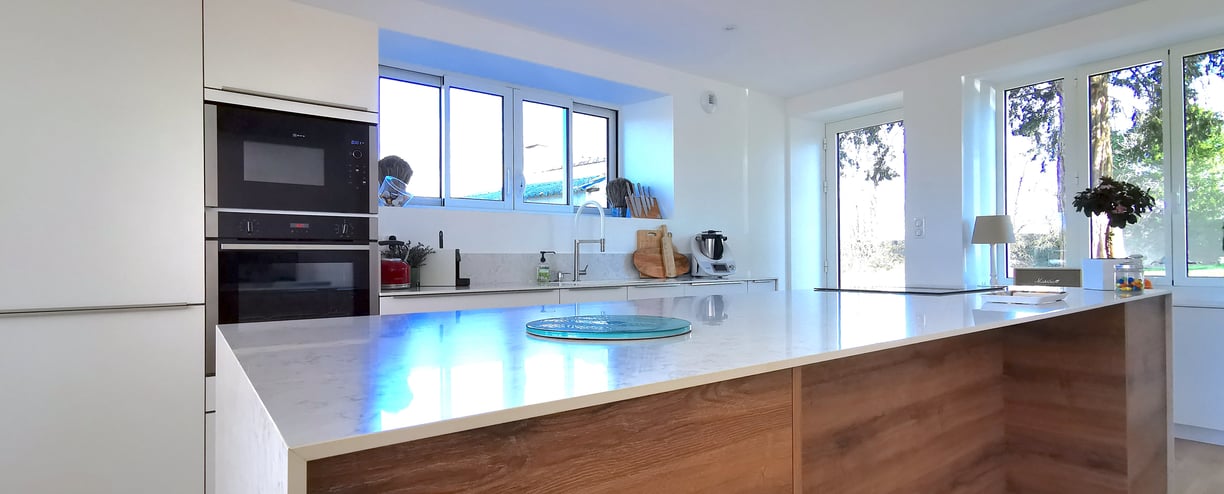 Cuisine blanche avec îlot en bois et plan de travail en marbre. Plaque de cuisson avec hotte intégré