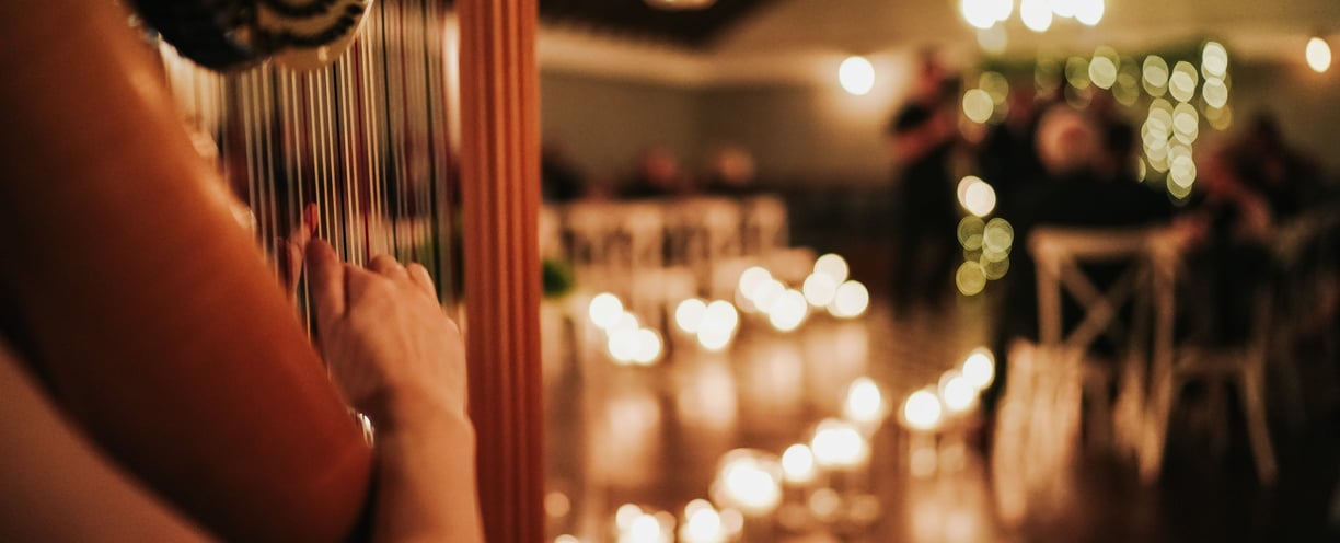 Wedding ceremony with room lit by numerous candles. Harp being performed is focus of the picture.