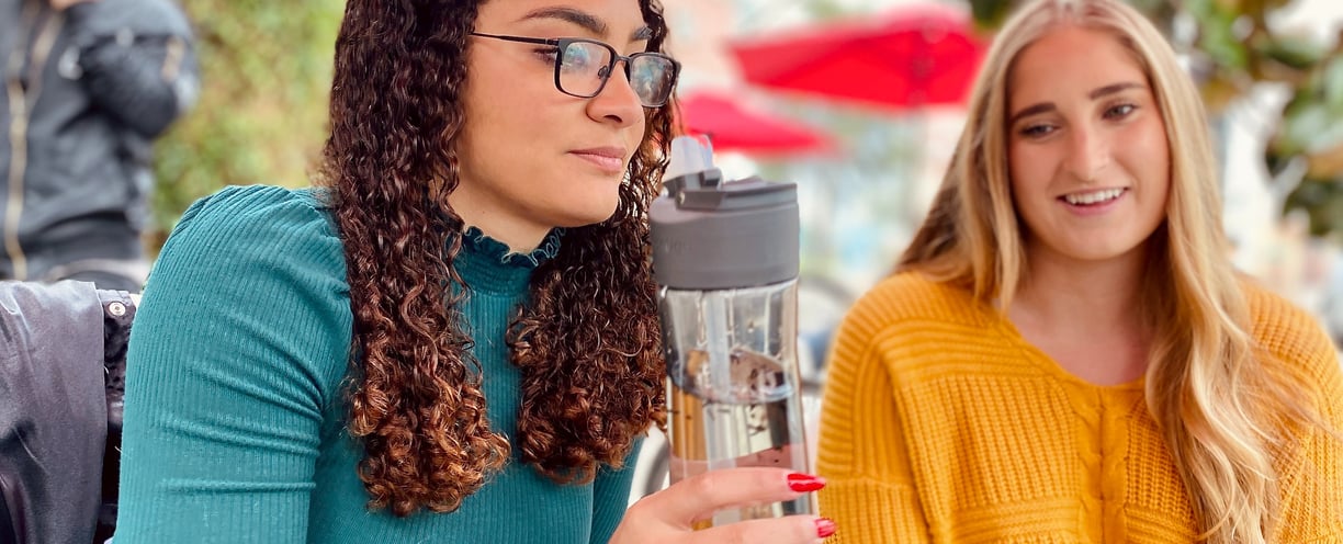 Two Girls talking and one is sipping a bottle of tea