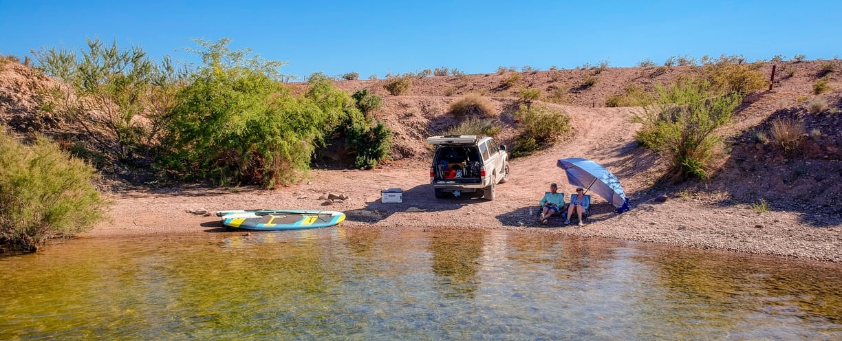 day camp setup on coloardo river with 4runner, 2 people, umbrella and paddle boards by the water