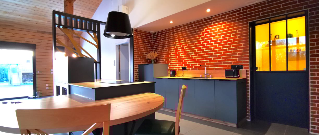 Cuisine vert foncé avec plan de travail en chêne. Mur en briques de parement. Ilot central et hotte