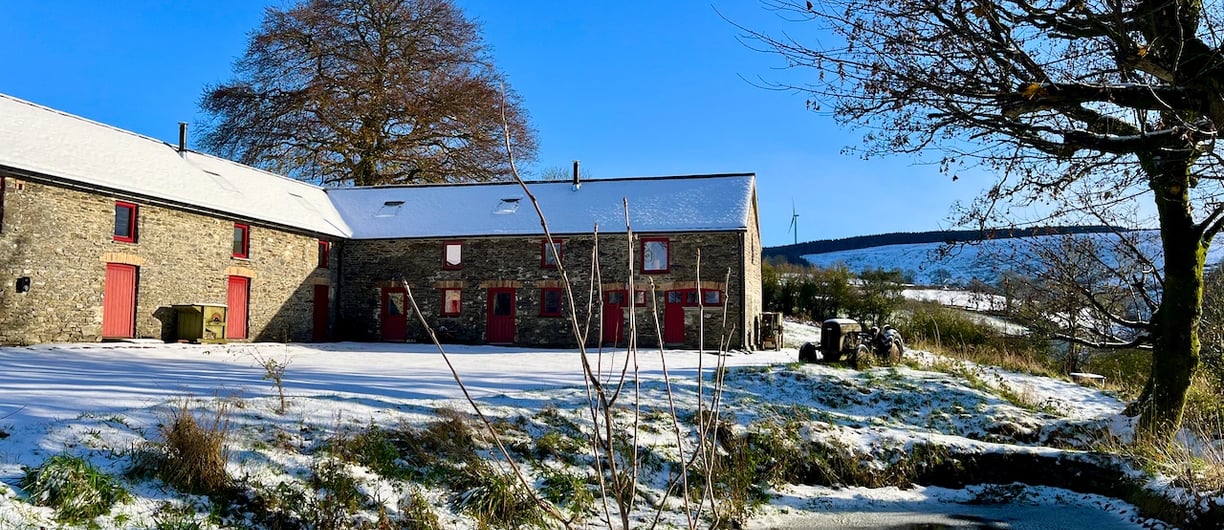 A large barn with a pond and in the snow with bright winter sunlight