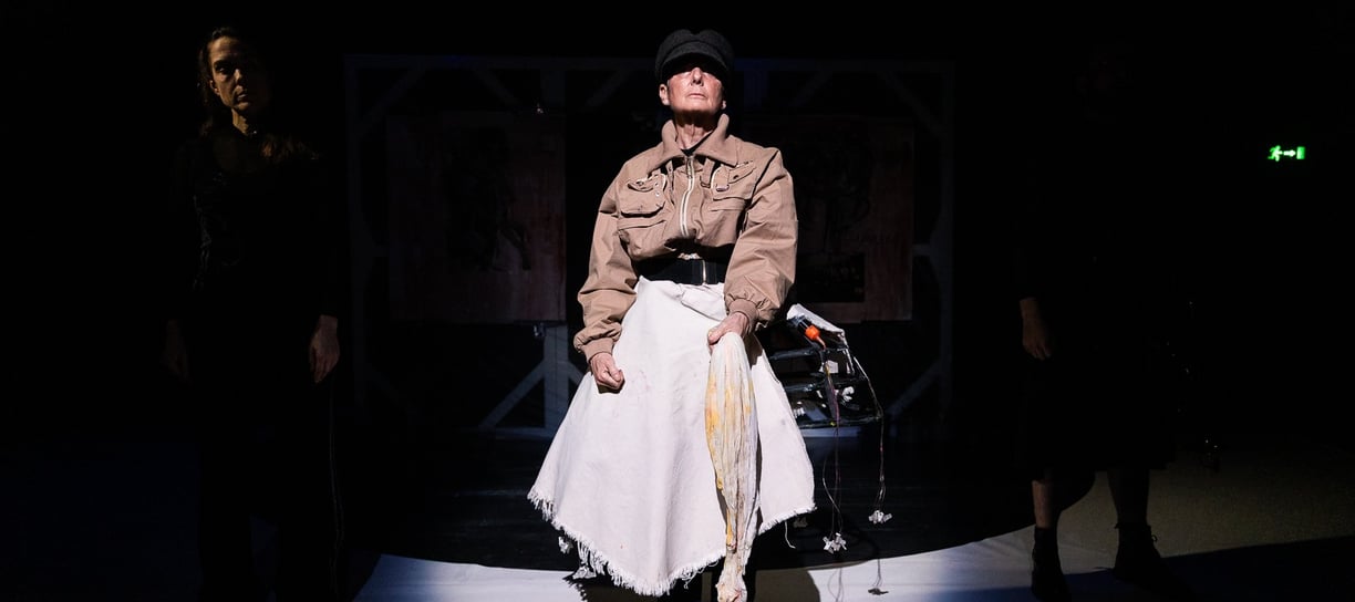 A white woman in a military cap and jacket, and white shirt, flanked by two very shaded people