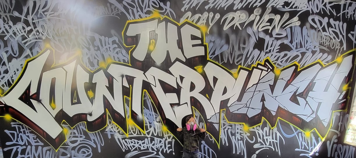 a kid standing in front of a graffiti - filled wall that reads "The Counterpunch"