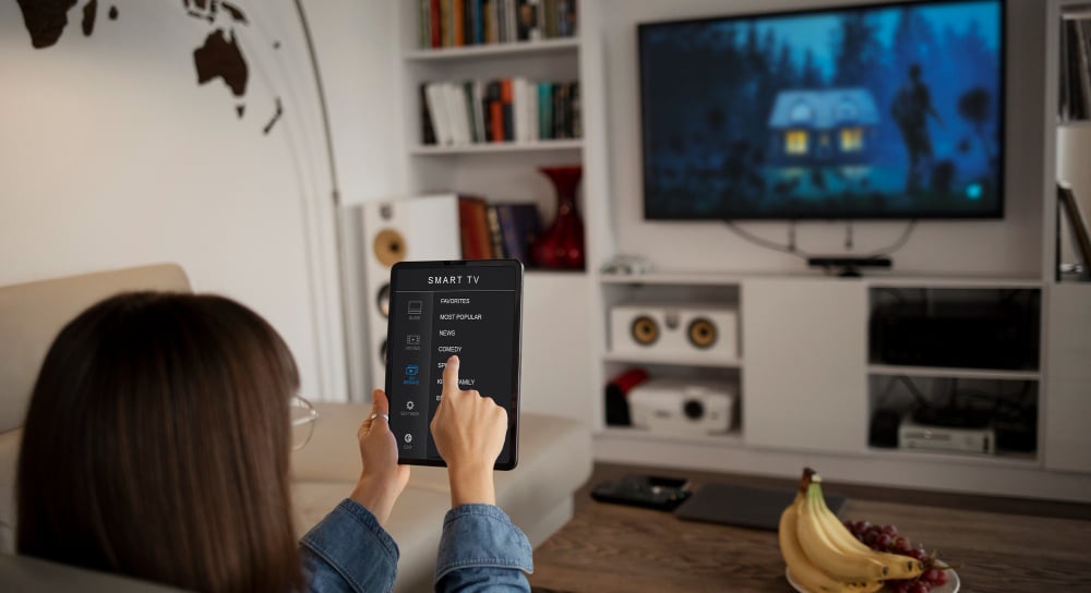 Woman holding a tablet computer and looking at a smart television for Morgan Hill TV installation.