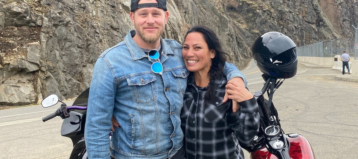 man with his arm around a woman with two motorcycles behind them