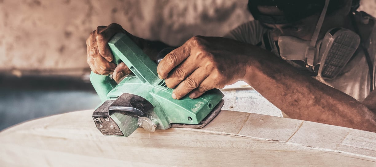 Craftsman shaping a handmade balsa surfboard with an electric planer