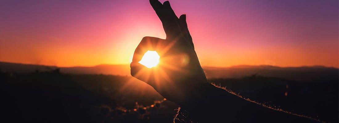 a person holding up a peace sign with the sun setting in the background