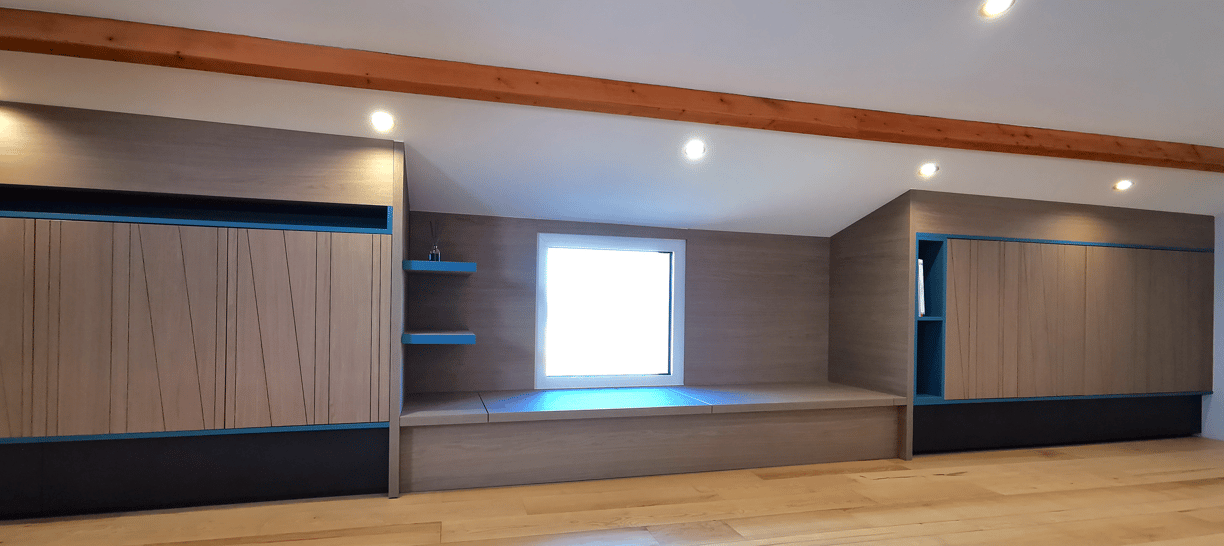 Aménagement sous combles en bois grisé et niches déco bleues. Banc avec rangement, portes usinées.