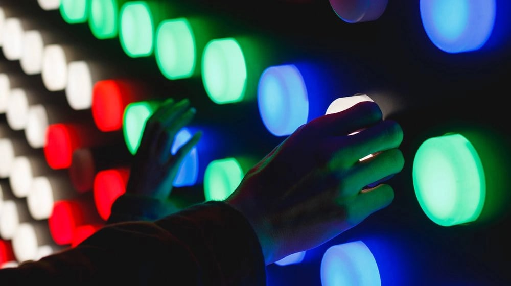 a person holding a remote control device in front of a wall of colored lights