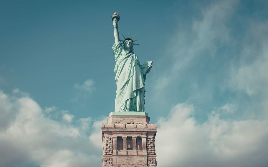 A close-up of the Statue of Liberty, standing tall with her torch raised against a clear blue sky.