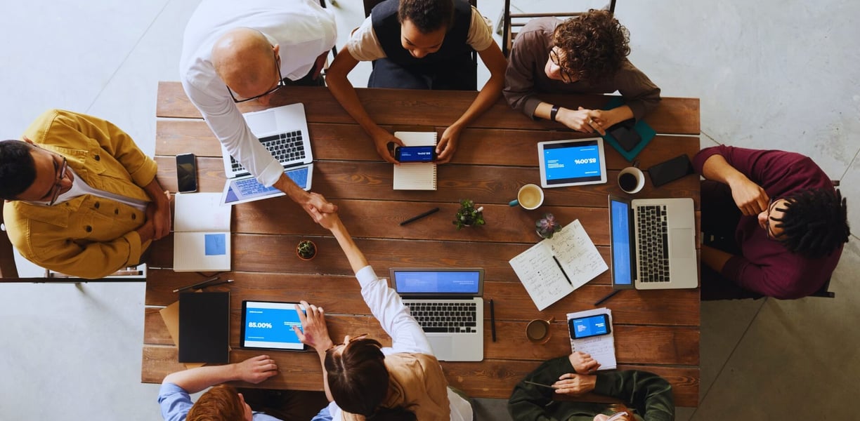 a group of people sitting around a table with laptops