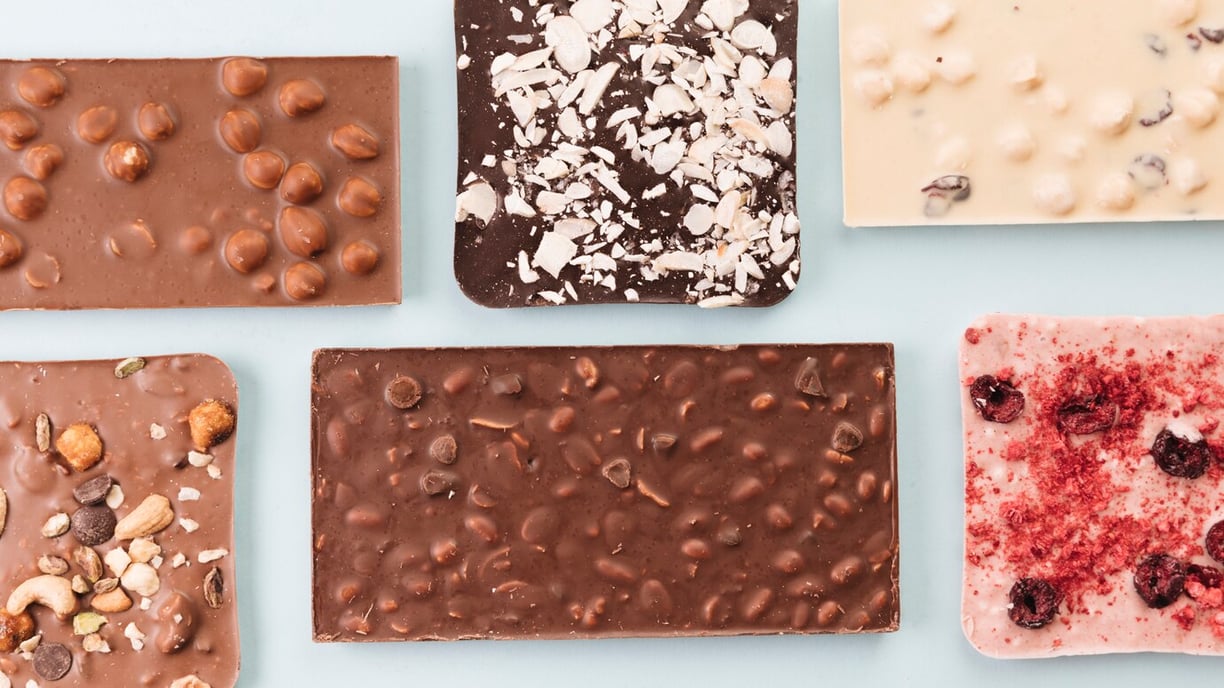 Top view of mixed white, milk, & dark chocolate bars with nuts & dried fruit pieces artfully arrange