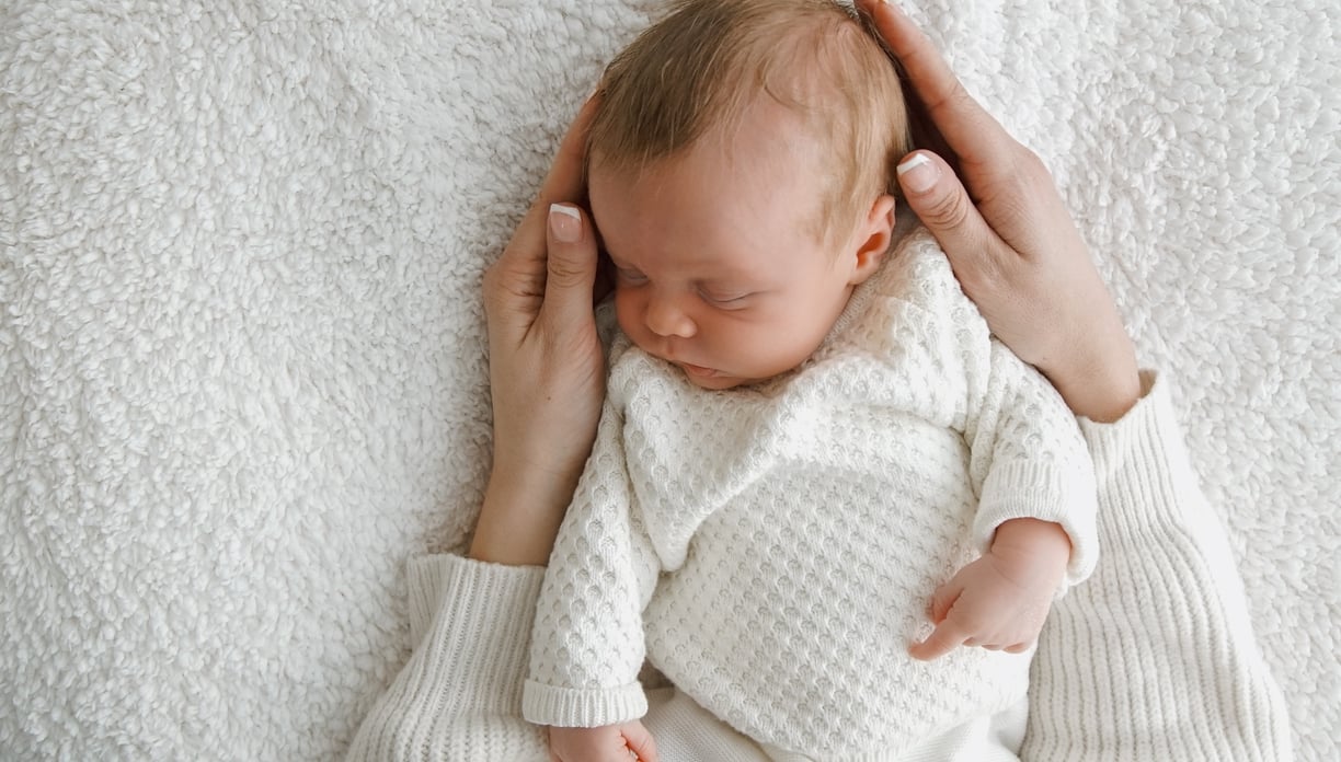 a baby is sleeping on a blanket and holding her hands up to her head