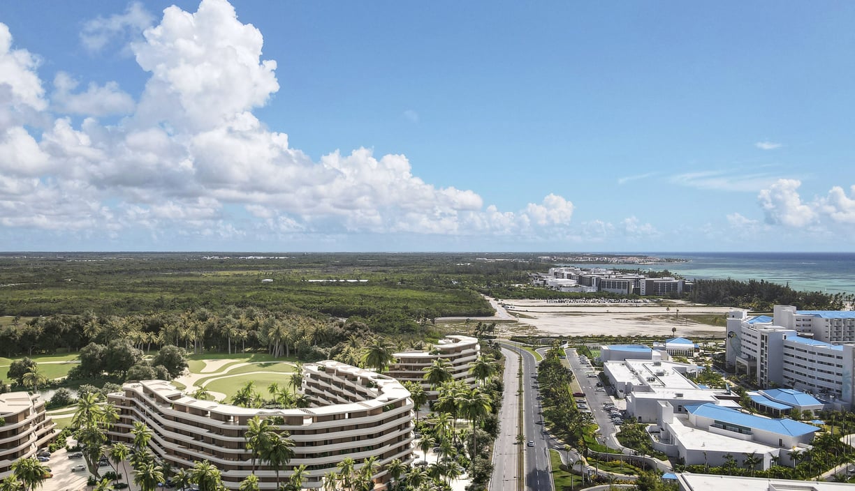 Luxury coastal resort with wave-like buildings, lush greenery, pools, a golf course, and ocean view.