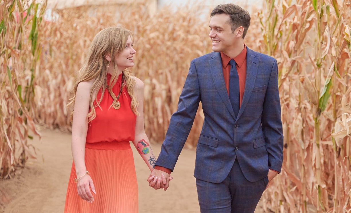 a man and woman holding hands and walking through a corn maze