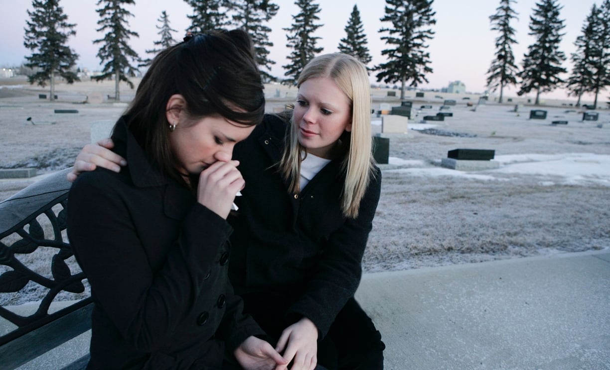 two women sitting on a bench in a cemetery