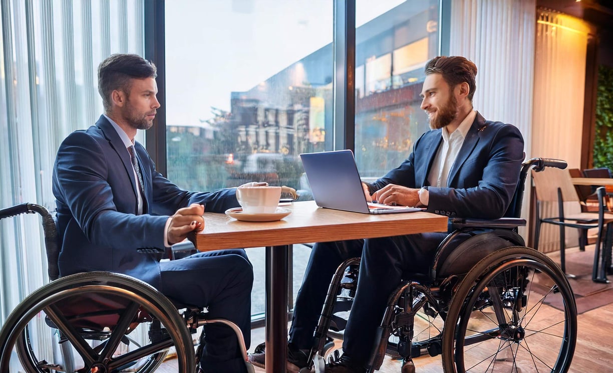 Zwei Rollstuhlfahrer sitzen für ein Beratungsgespräch in einem Café