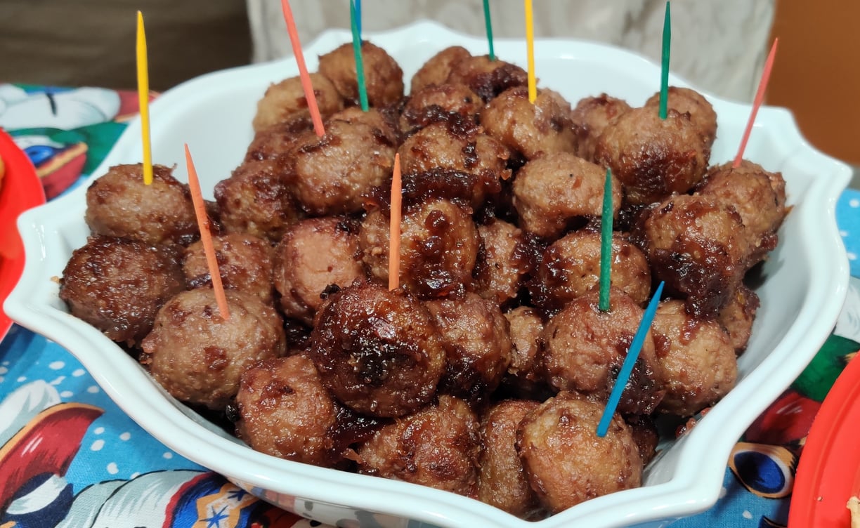 A bowl of crockpot meatballs with colorful toothpicks sticking out on a Christmas tablecloth