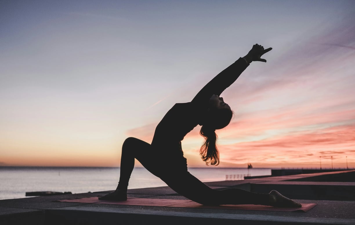 Woman practicing yoga at sunrise by the water, symbolizing peace and natural harmony