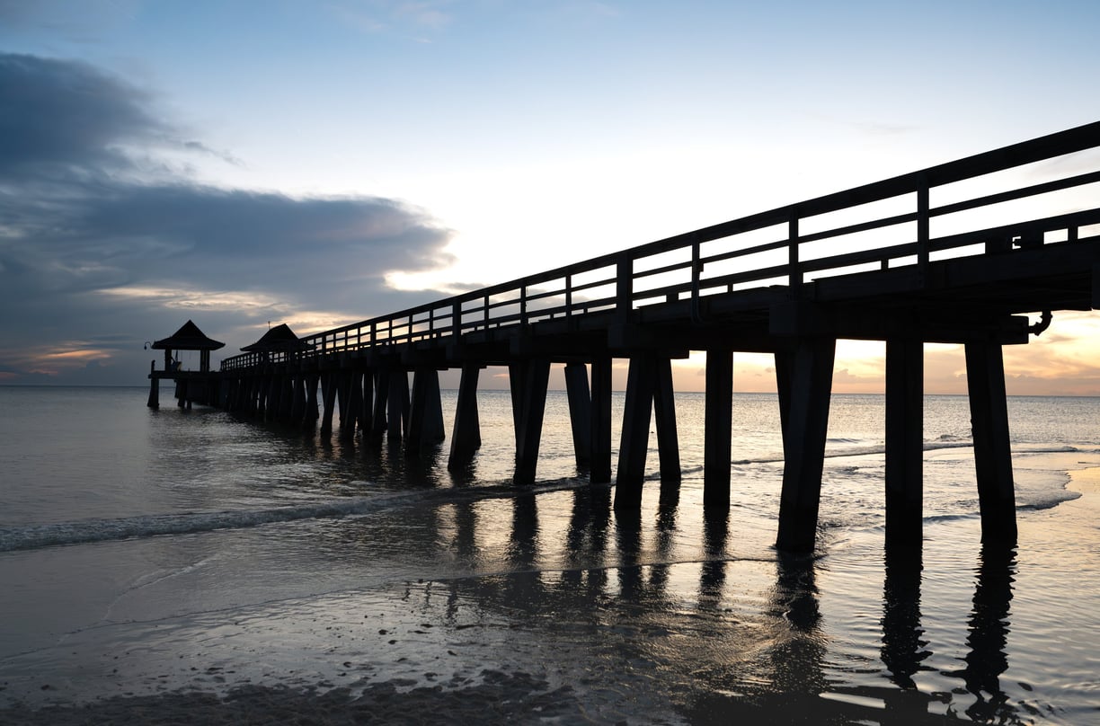 shadowy sunset view of naples pier in naples florida, with waves and the ocean and clouds 